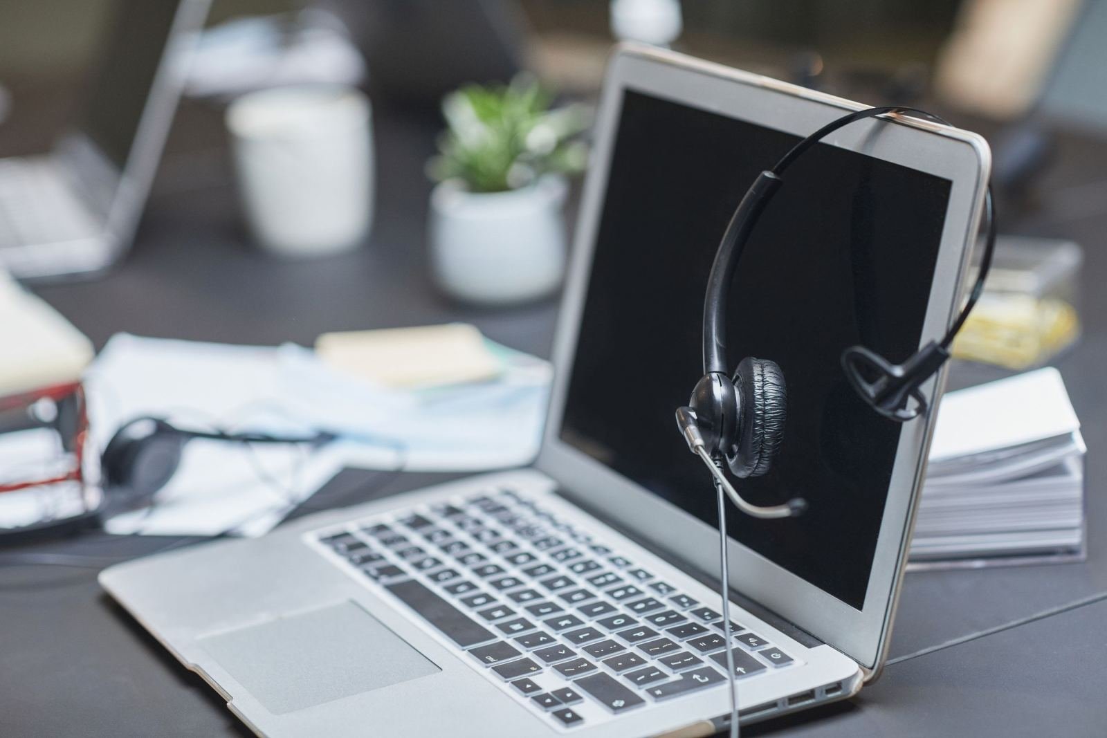 A laptop with a headset resting on the screen on an office desk