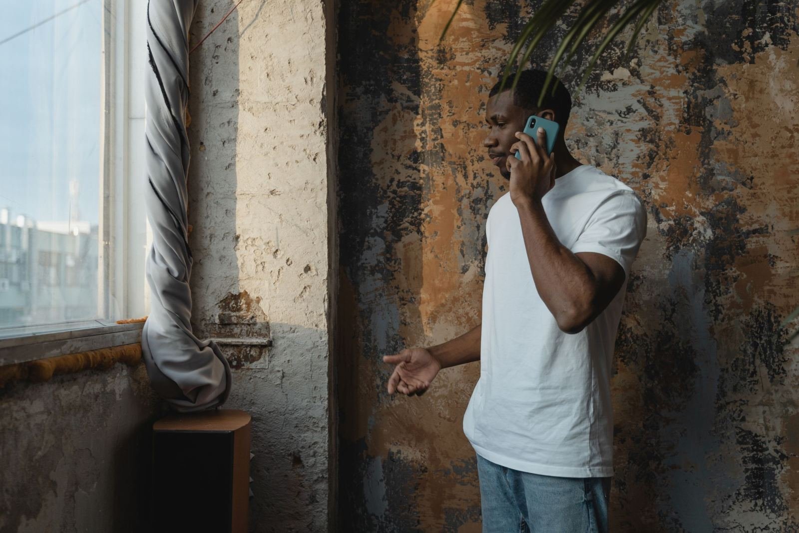 A man in a white t-shirt talks on a blue smartphone against a textured wall