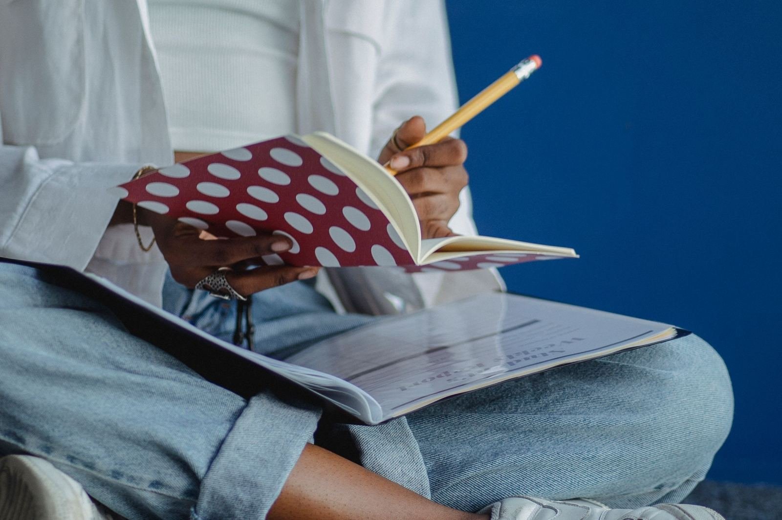 A person sitting cross-legged writing in a polka-dot notebook