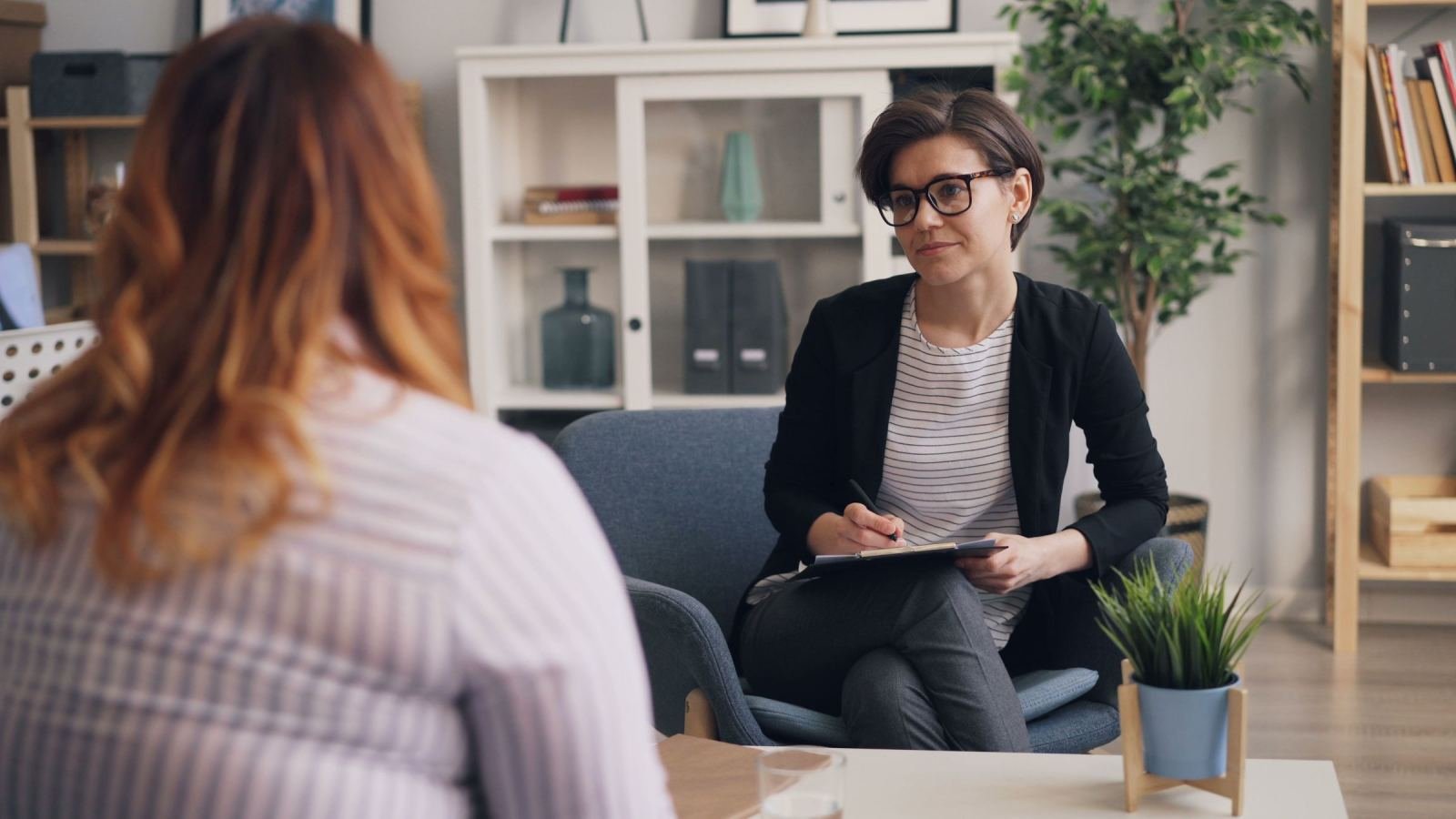 A professional woman with a clipboard listens to a client in a modern office