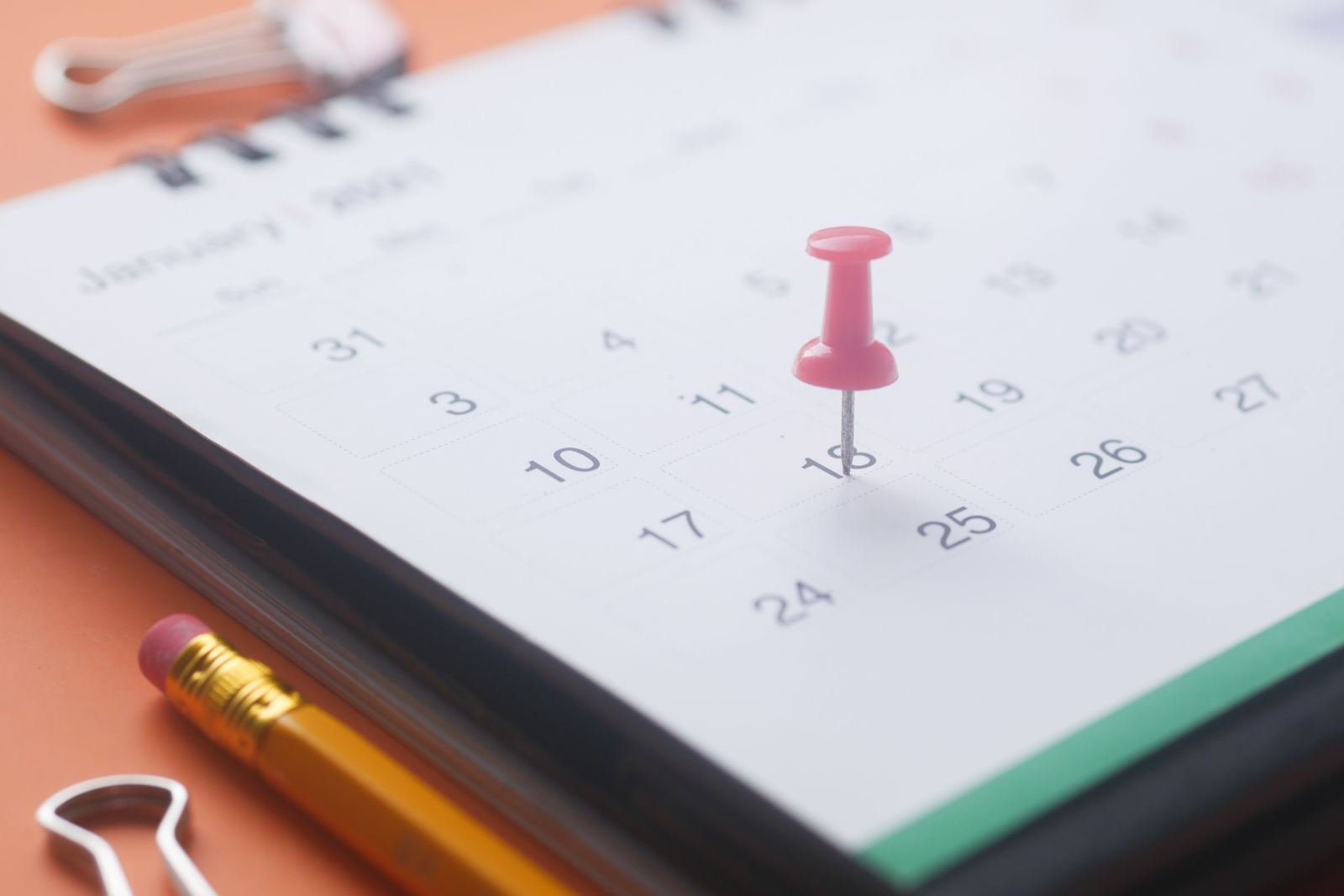 A red pushpin marks a date on a white calendar next to a yellow pencil