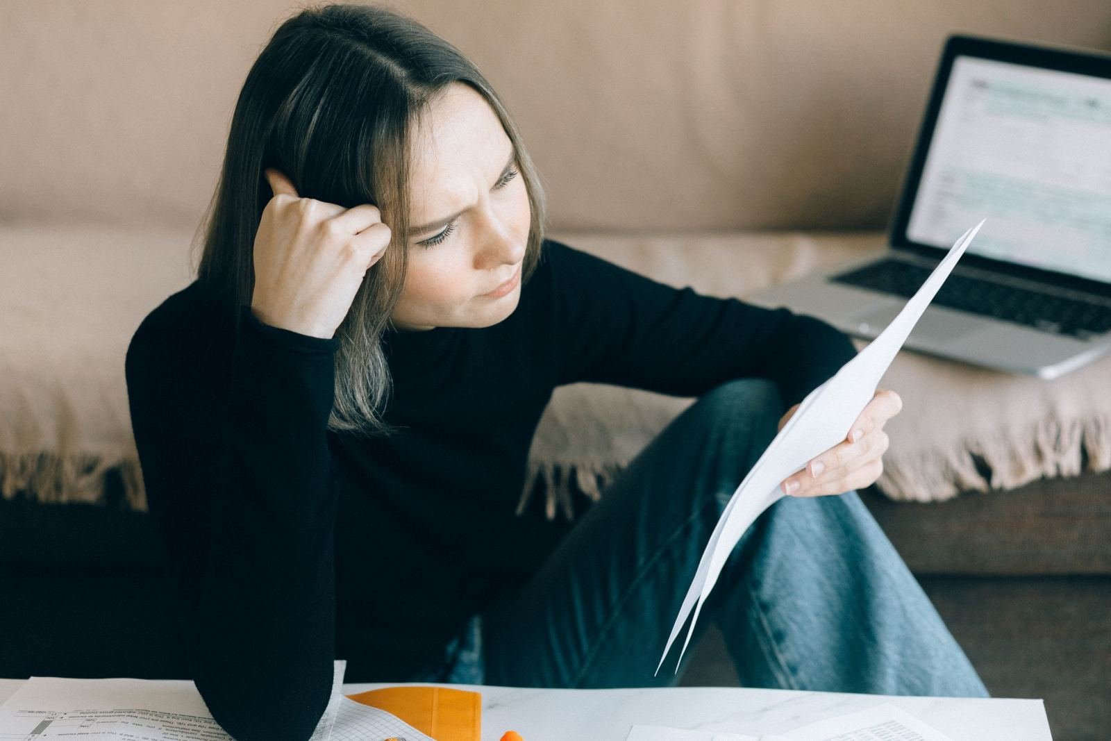 A woman sits on the floor reading a document with a serious expression