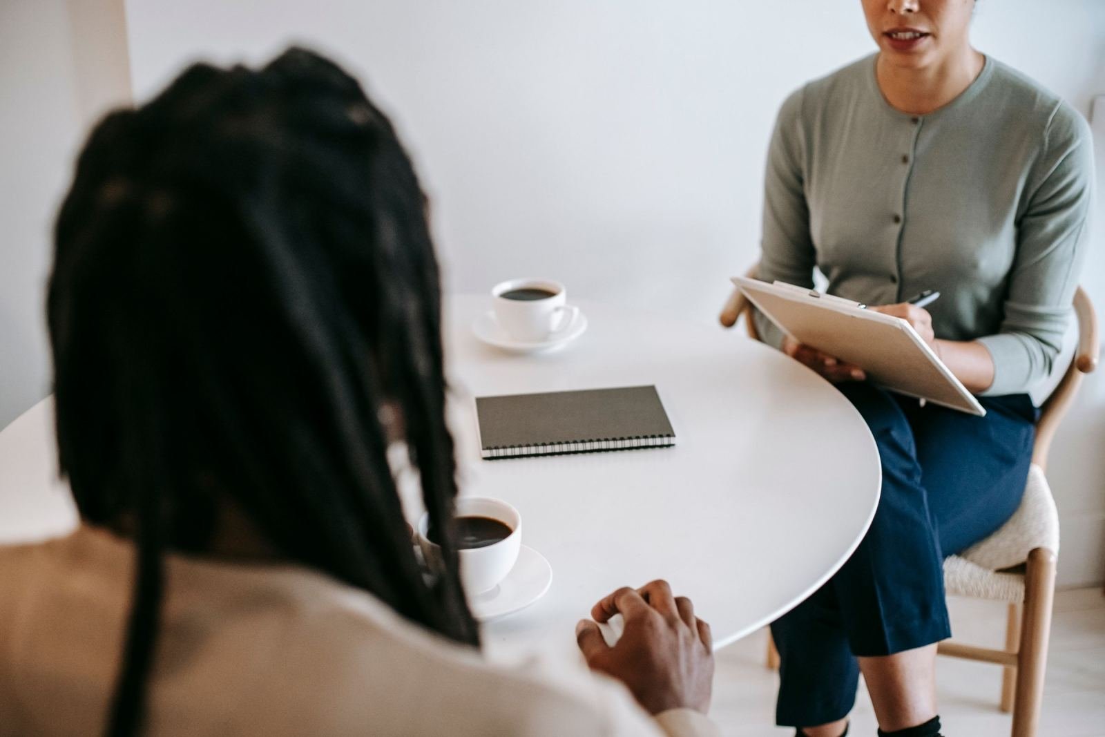 A care provider with a clipboard talks to a client across a white table