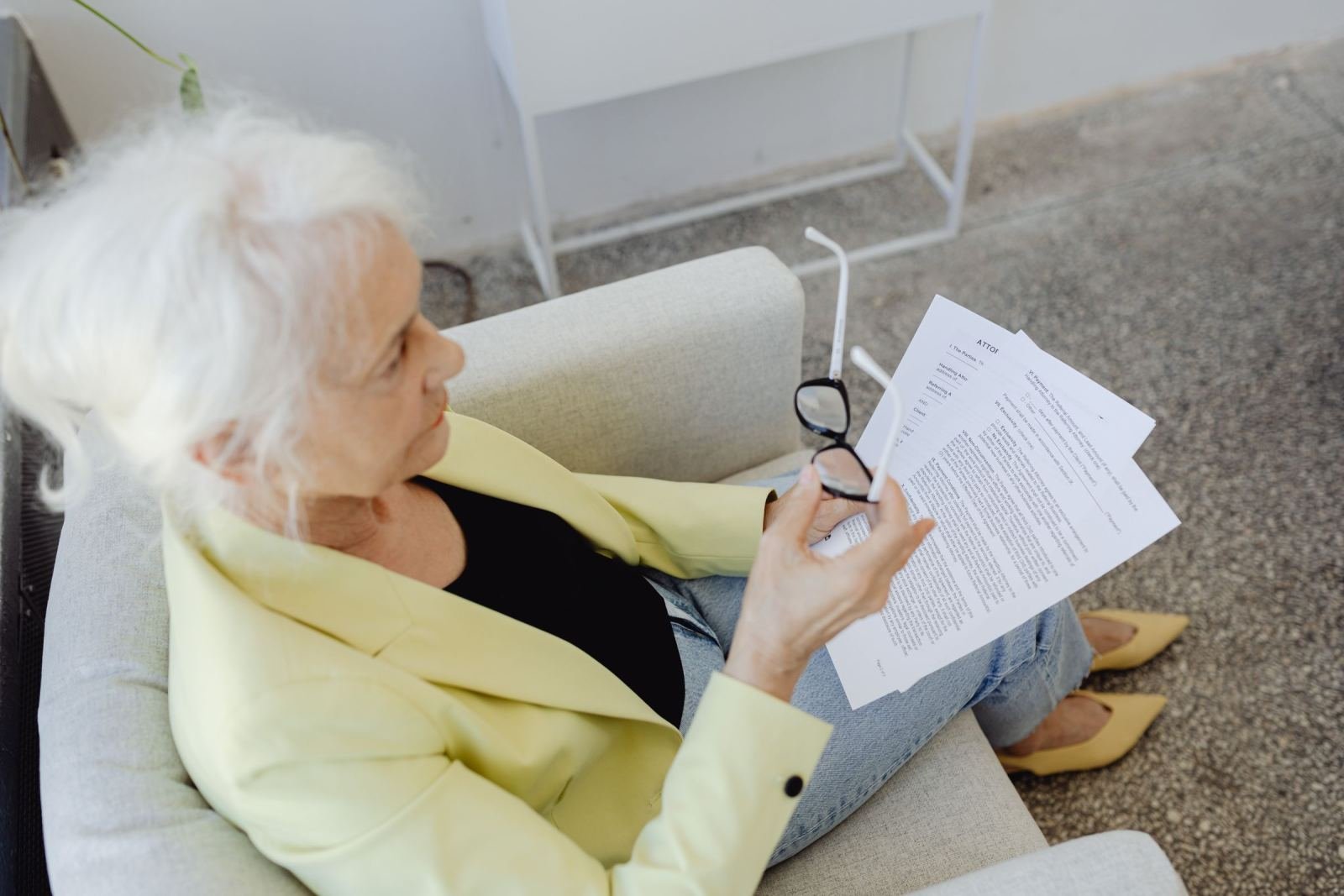 A woman in a yellow blazer sits in an armchair reading a document