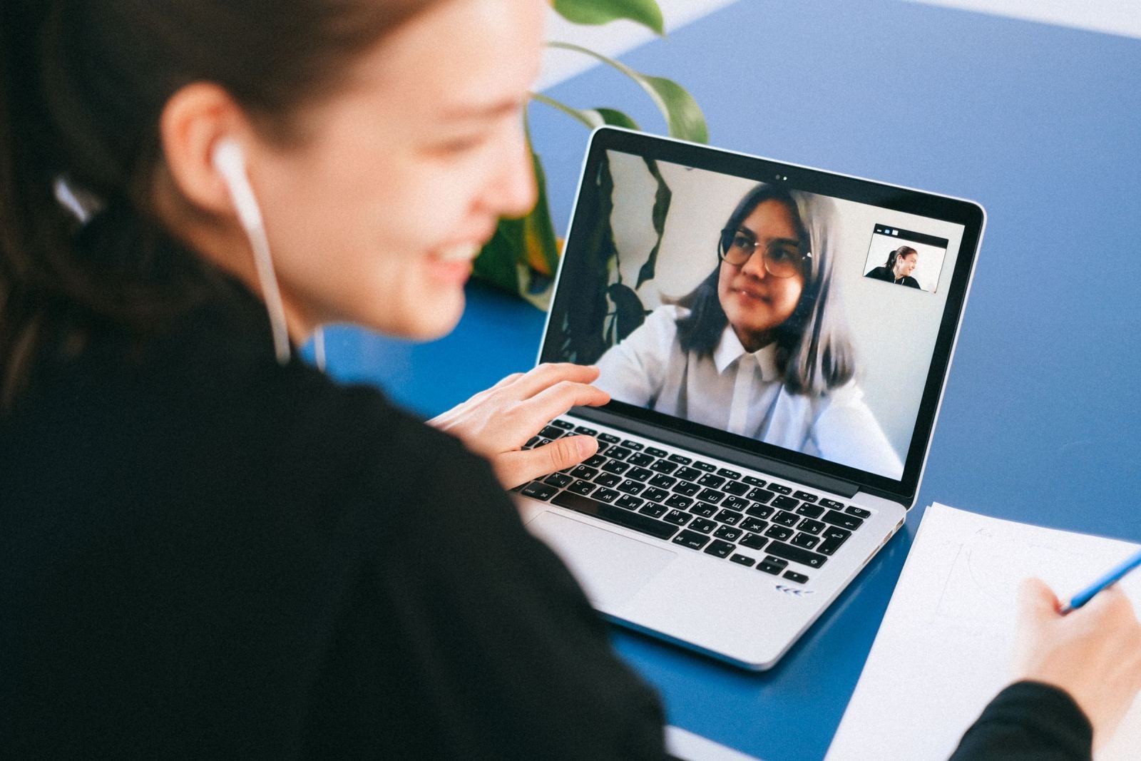 A woman wearing earbuds participates in a video call with two other people on her laptop