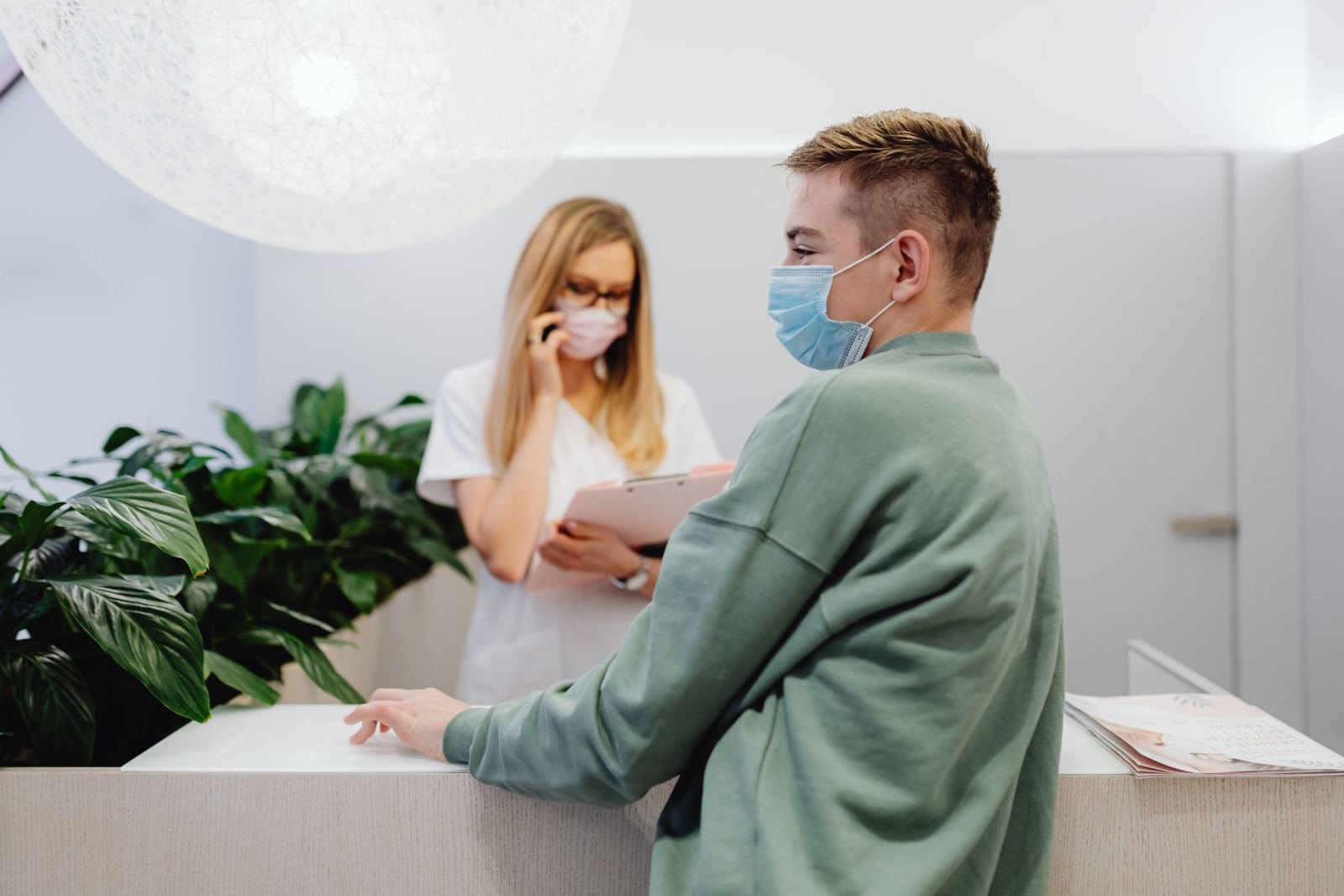 A masked man speaks with a medical professional at a clinic front desk.
