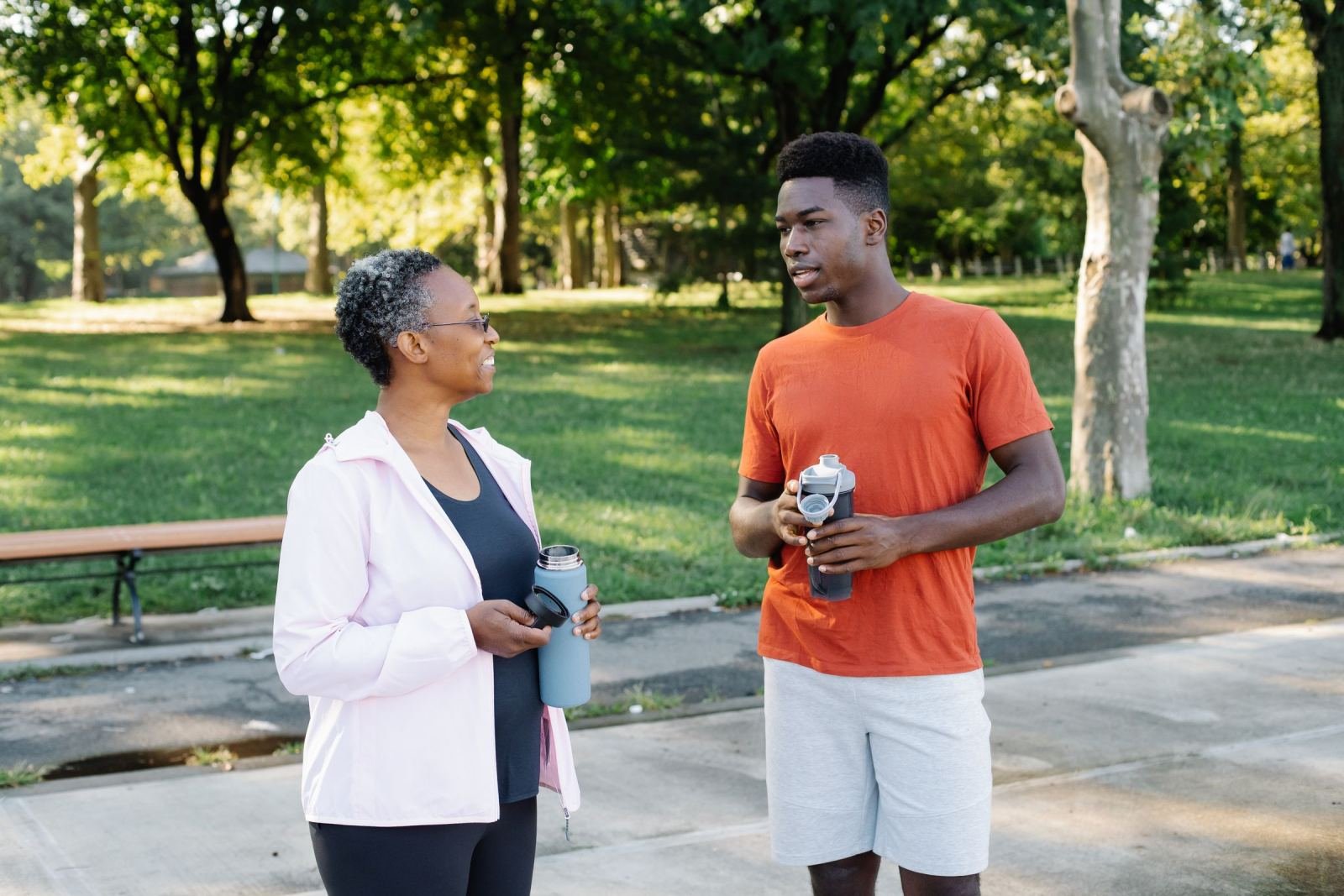 On a paved path in a park, a man and a woman walk side by side, talking.