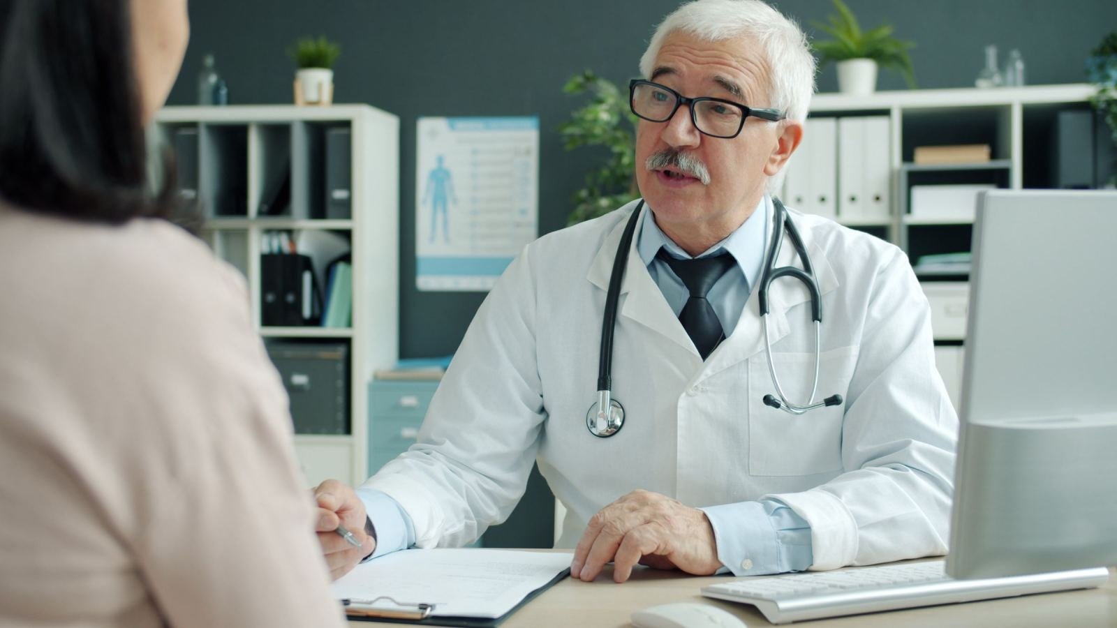 A patient talks with a doctor in a white coat at a medical office.