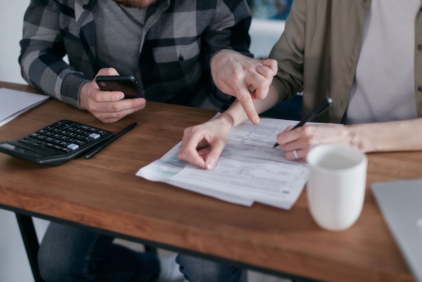 Two people review a document and use a calculator at a wooden desk