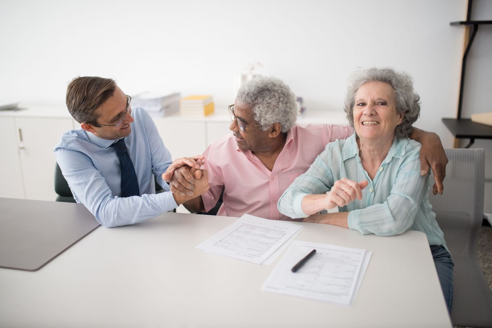 A professional man shakes hands with an older man while an older woman smiles beside them