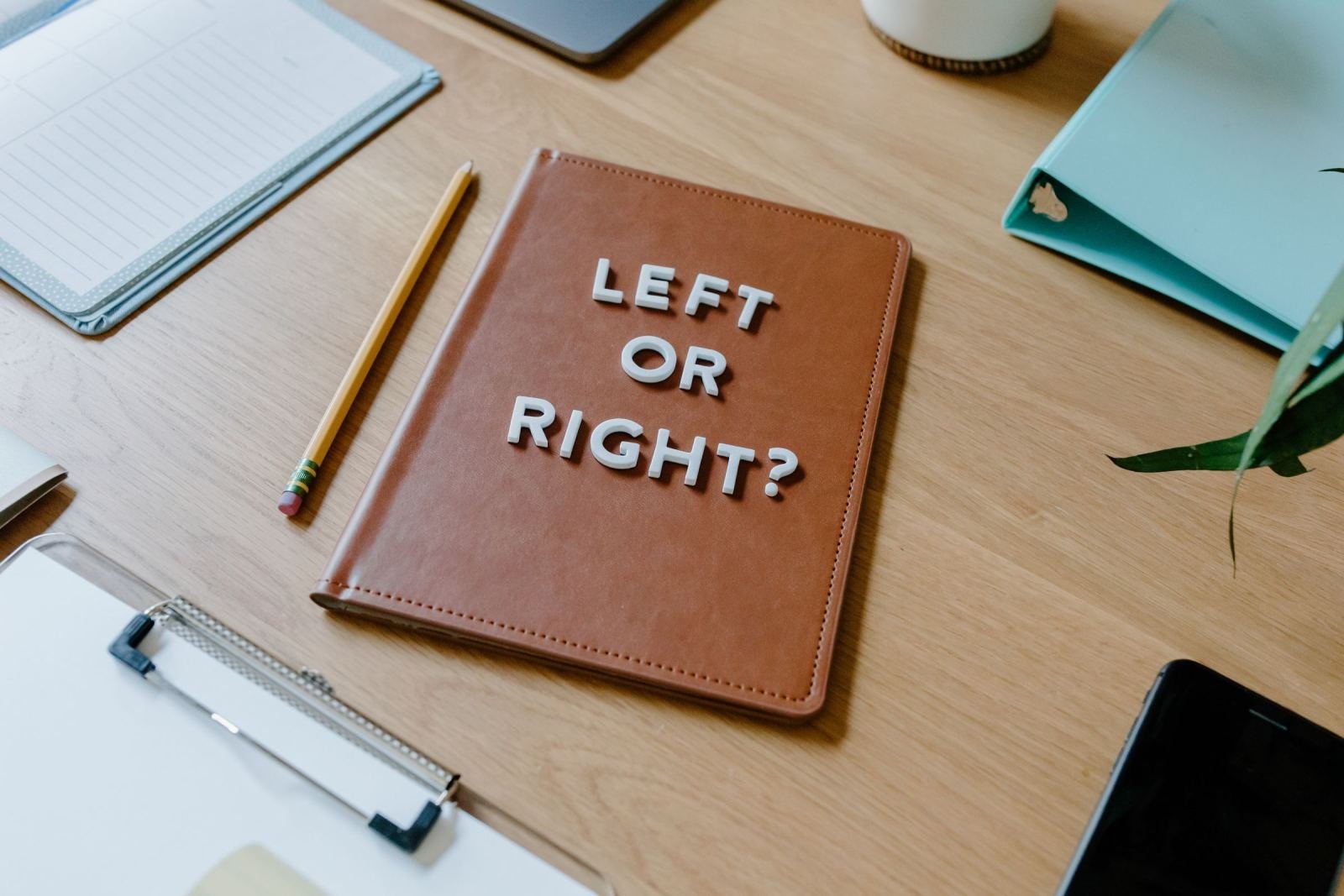 A brown notebook on a wooden desk with the words 'LEFT OR RIGHT?' on the cover
