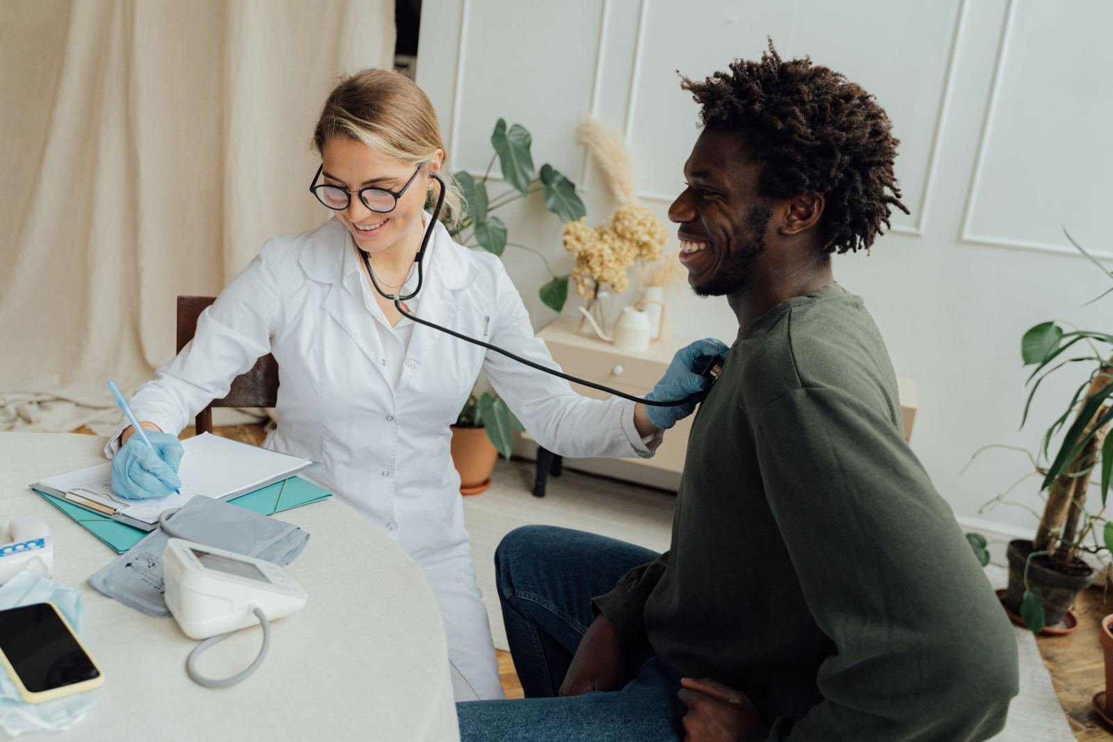 A man smiles while a doctor in a white coat listens to him with a stethoscope.