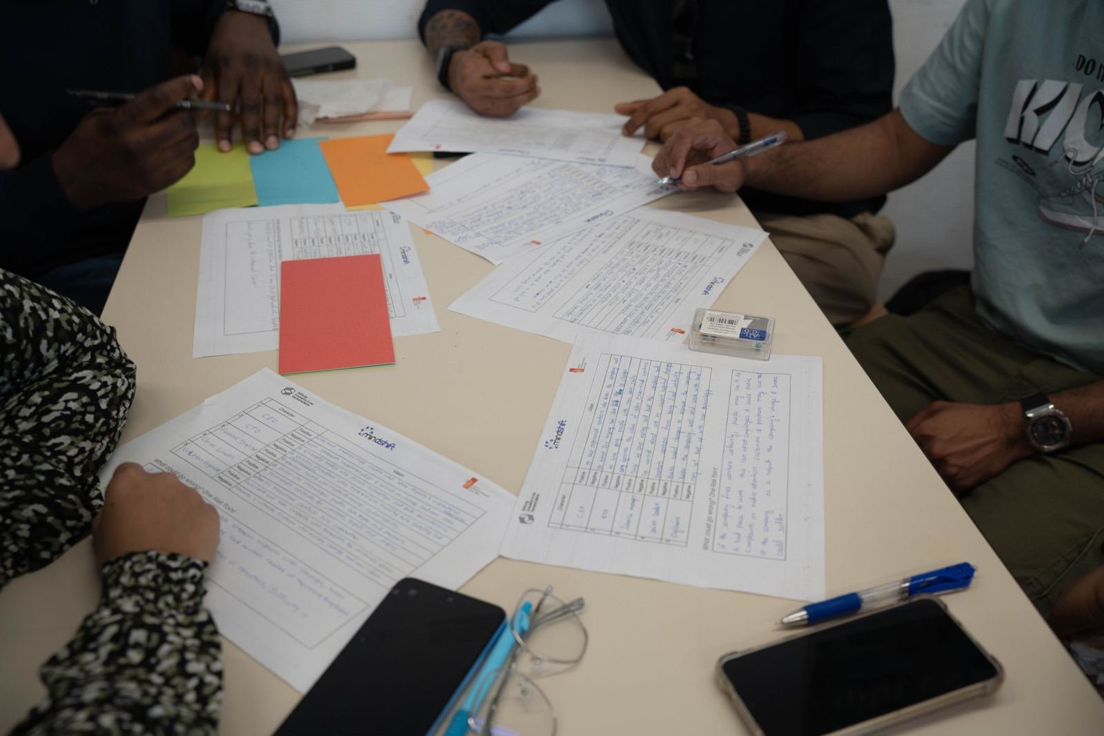 Three people look at papers and hand-written lists on a white table.