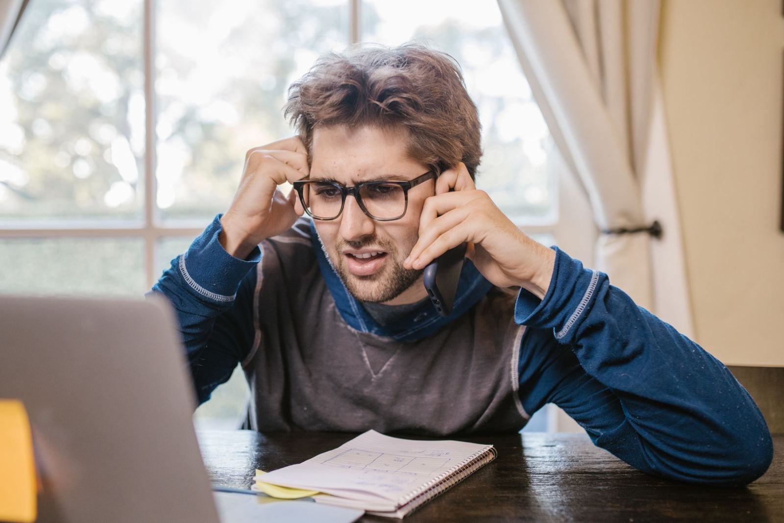 A man with glasses holds his head in frustration while sitting at a laptop