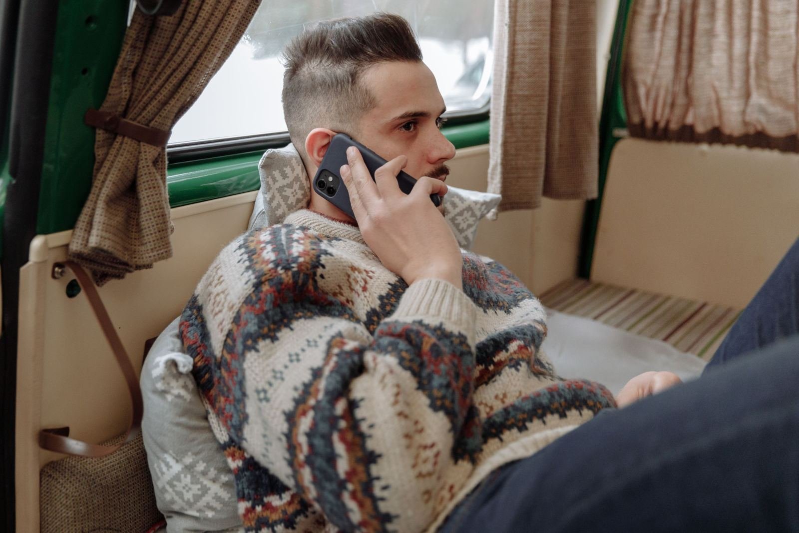 A man in a patterned sweater talks on a mobile phone while sitting in a vehicle